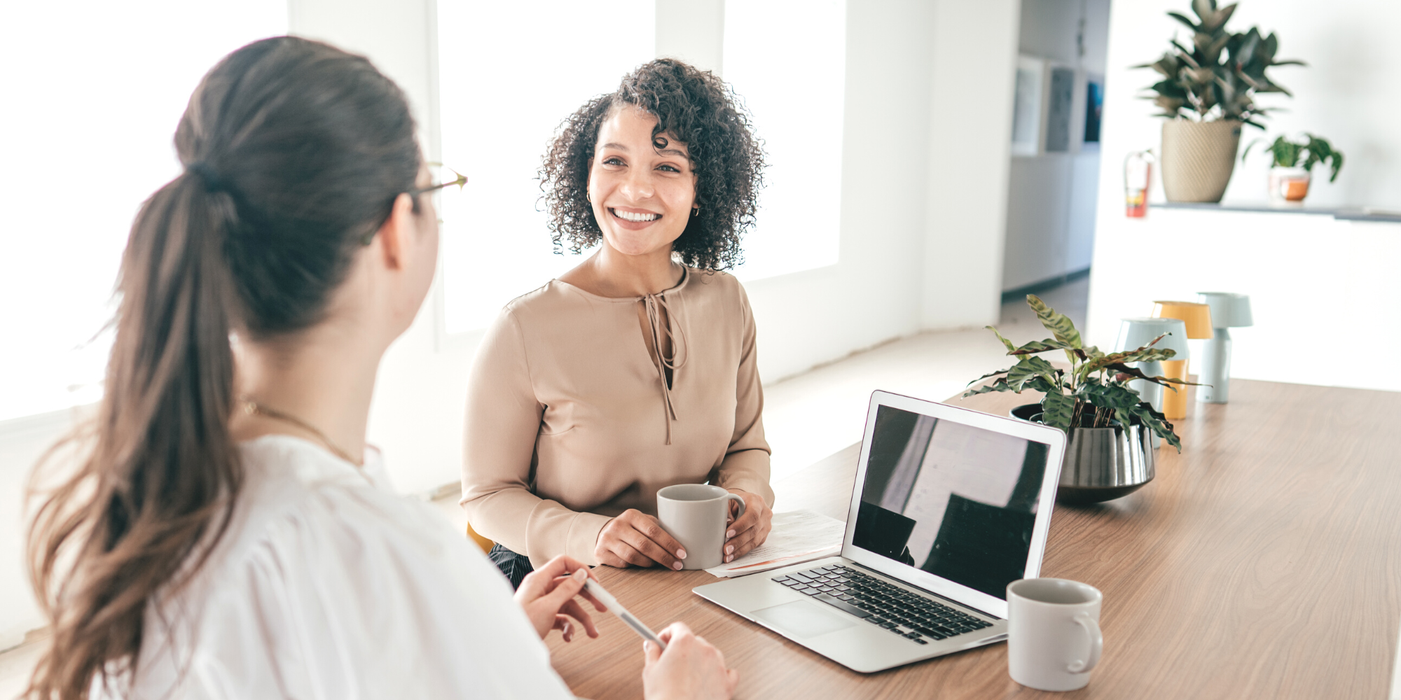 2 women talking with laptop and cup of coffee in office